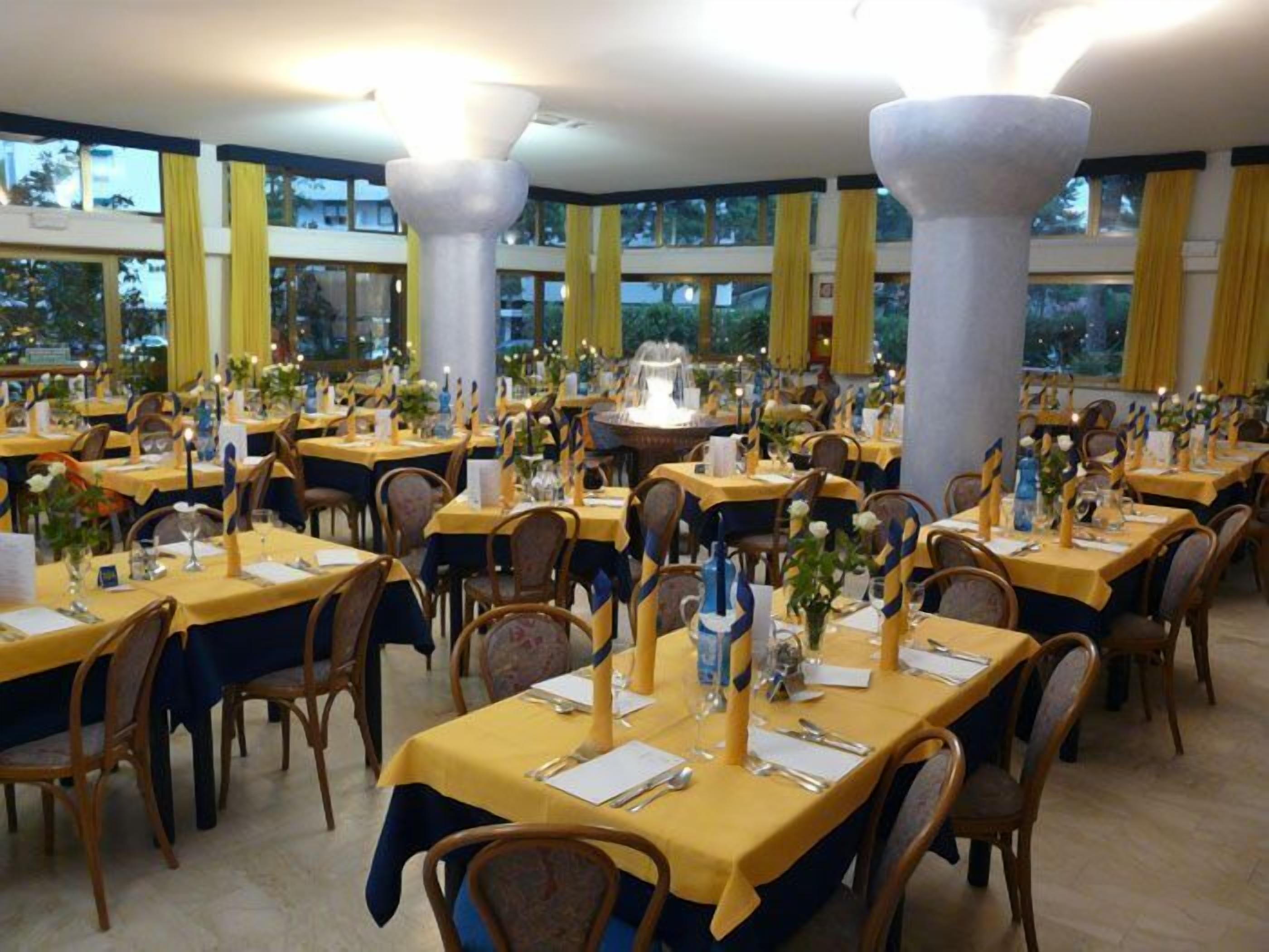 Un salón de banquetes con varias mesas dispuestas para comer, con manteles amarillos y sillas de madera.