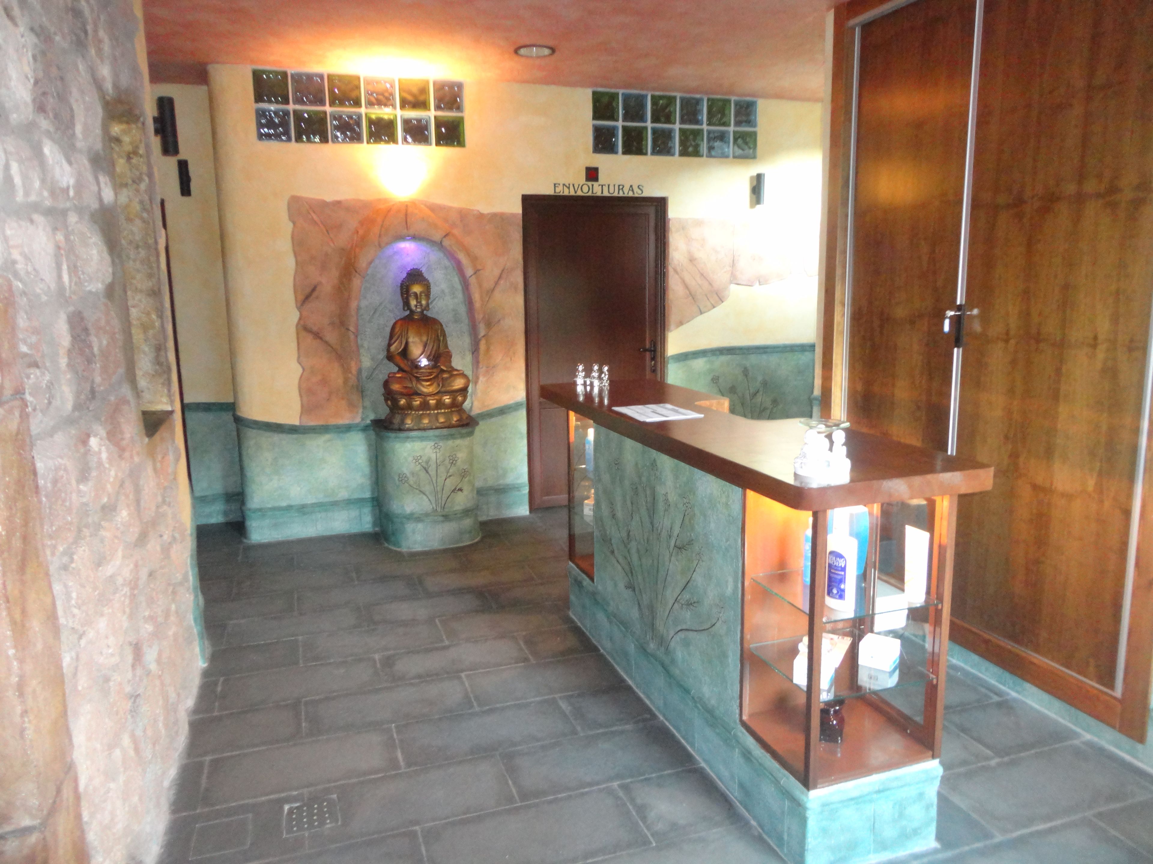 A room with a Buddha statue, a reception desk, and a wall with a mosaic.