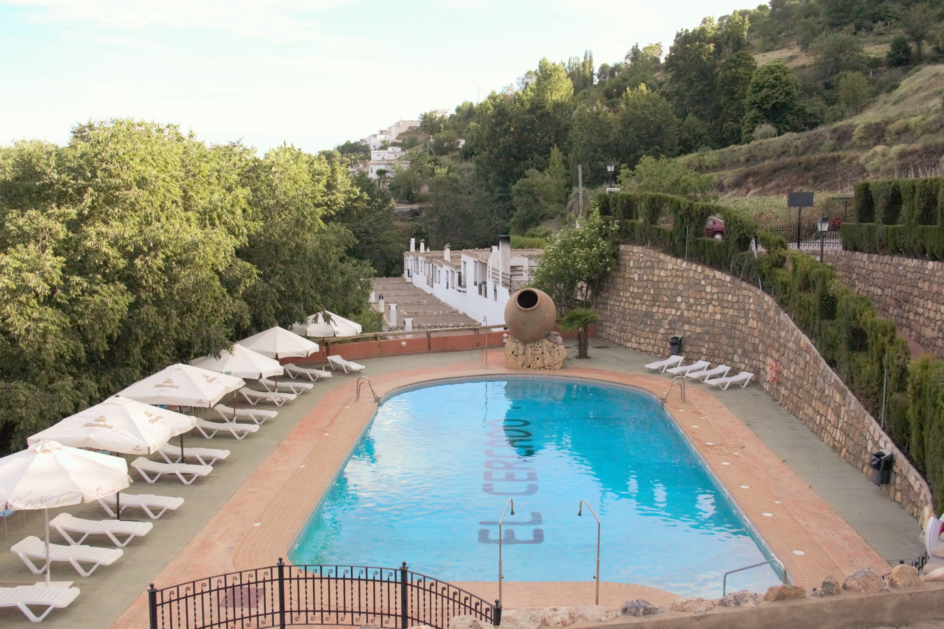 A swimming pool with lounge chairs and umbrellas, surrounded by stone walls and greenery.