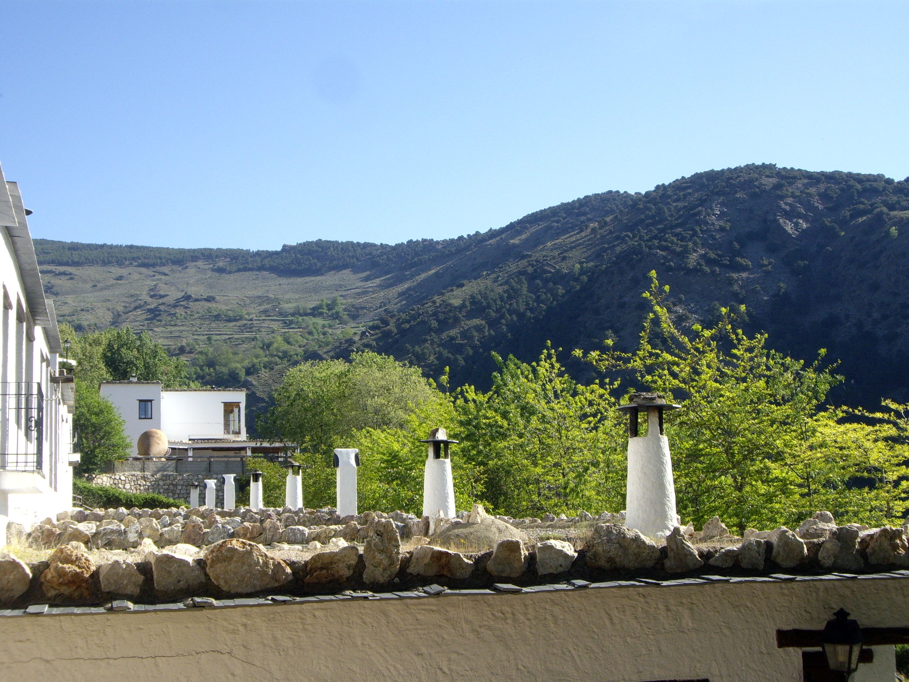 Paisatge costaner amb edificis blancs, un mur de pedra i un turó al fons.