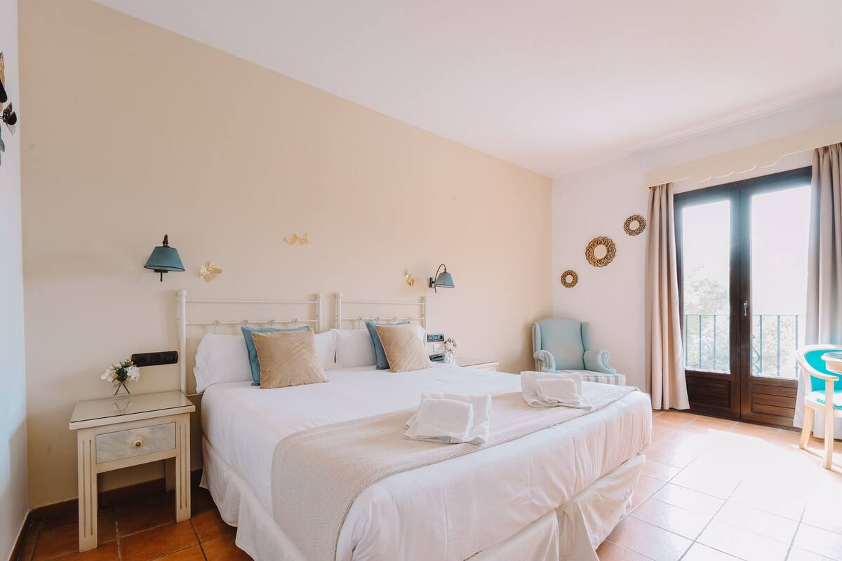 A hotel room with a large bed, two bedside tables, a chair, and a balcony with a view.