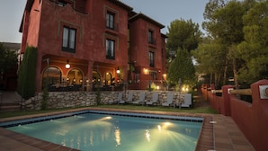 A poolside area with a pool, lounge chairs, and a building with a stone wall and a balcony. - Hotel Boutique Cerro del Sol (Cenes de la Vega)