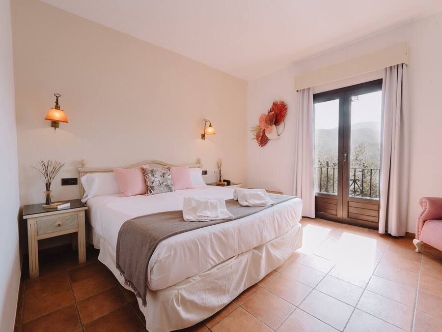 Un dormitorio con una cama grande, dos mesitas de noche, una mesita auxiliar, una ventana con vistas y un balcón.