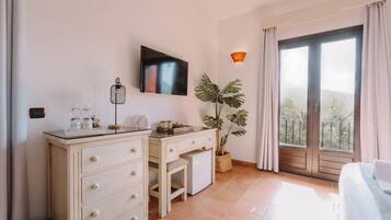 A hotel room with a desk, a large potted plant, a TV, and a balcony with a view.