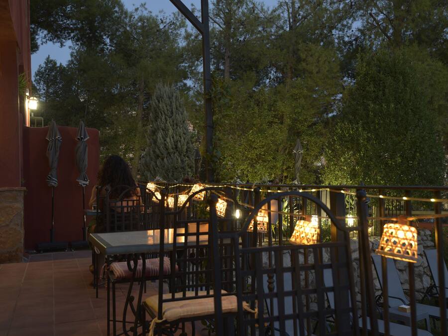 Un patio al aire libre con mesas y sillas, luces colgantes y un muro de piedra.