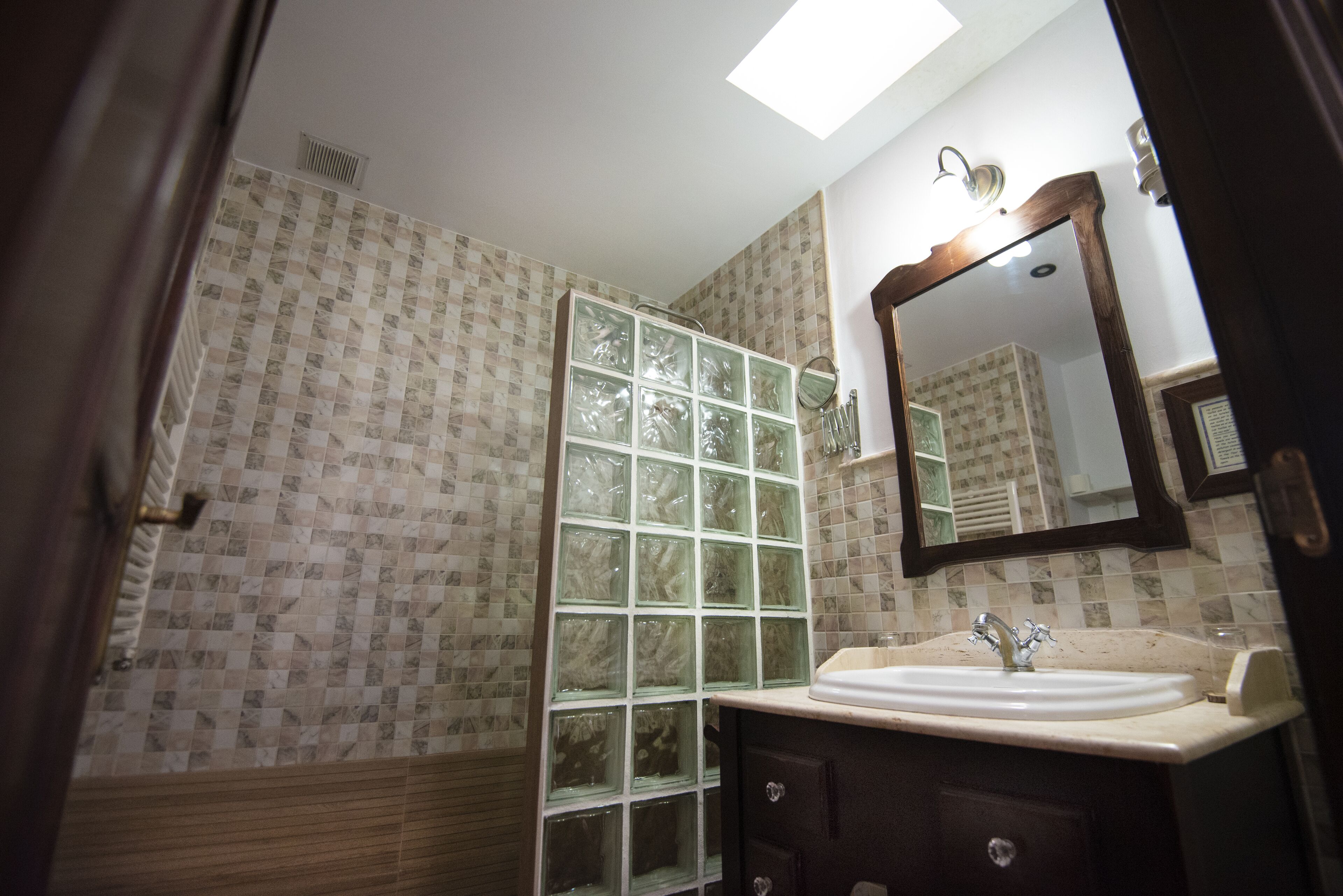 A bathroom with a tiled wall, a glass shower enclosure, a sink with a mirror, and a wooden door.