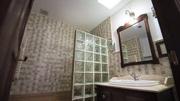 A bathroom with a tiled wall, a glass shower enclosure, a sink with a mirror, and a wooden door.