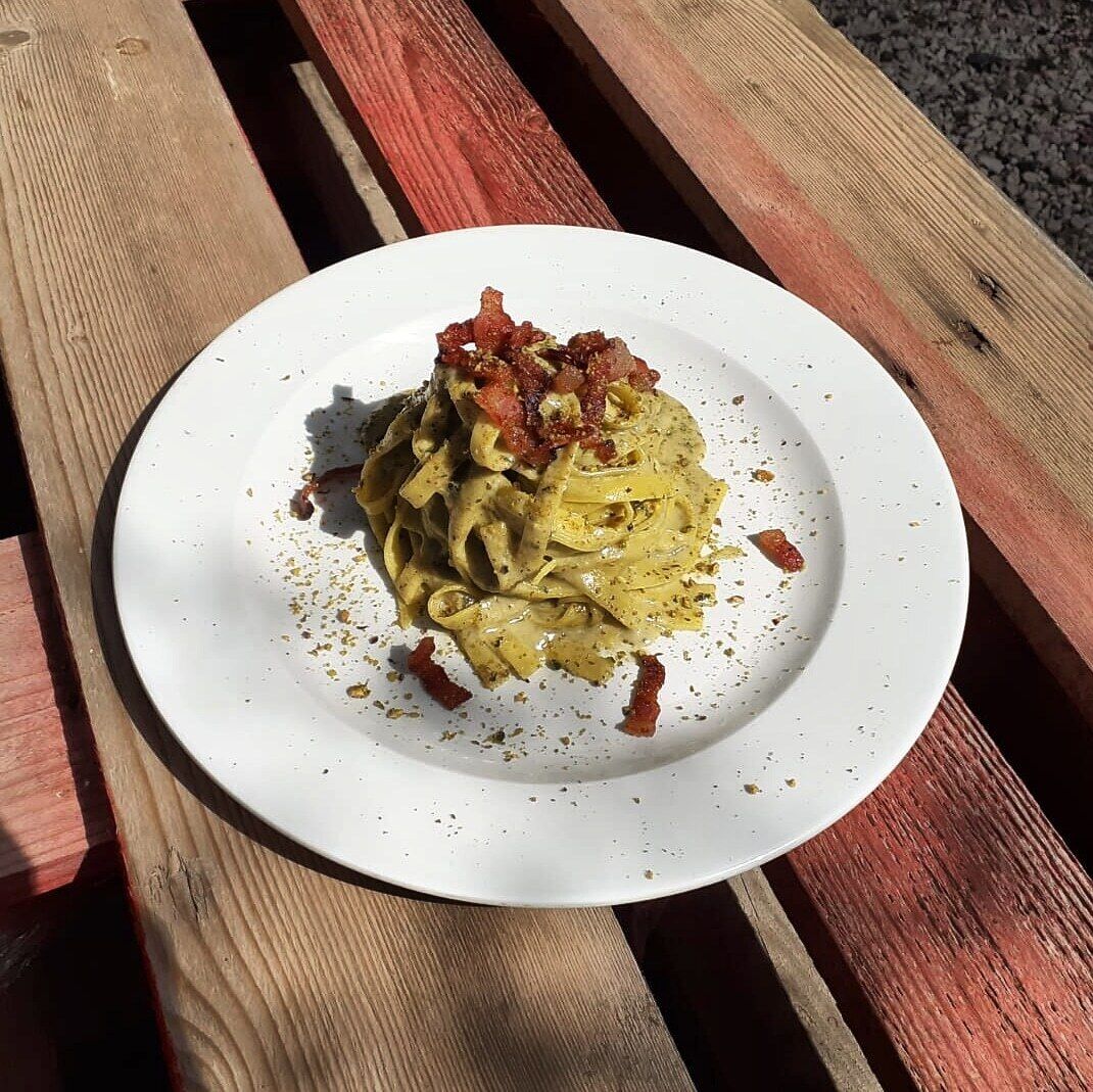 A plate of pasta with a creamy sauce and crispy bacon on a wooden bench.