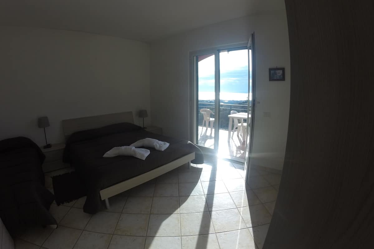 Ein Hotelzimmer mit Bett, Nachttisch, Tisch mit Stühlen und einem Balkon mit Aussicht.
