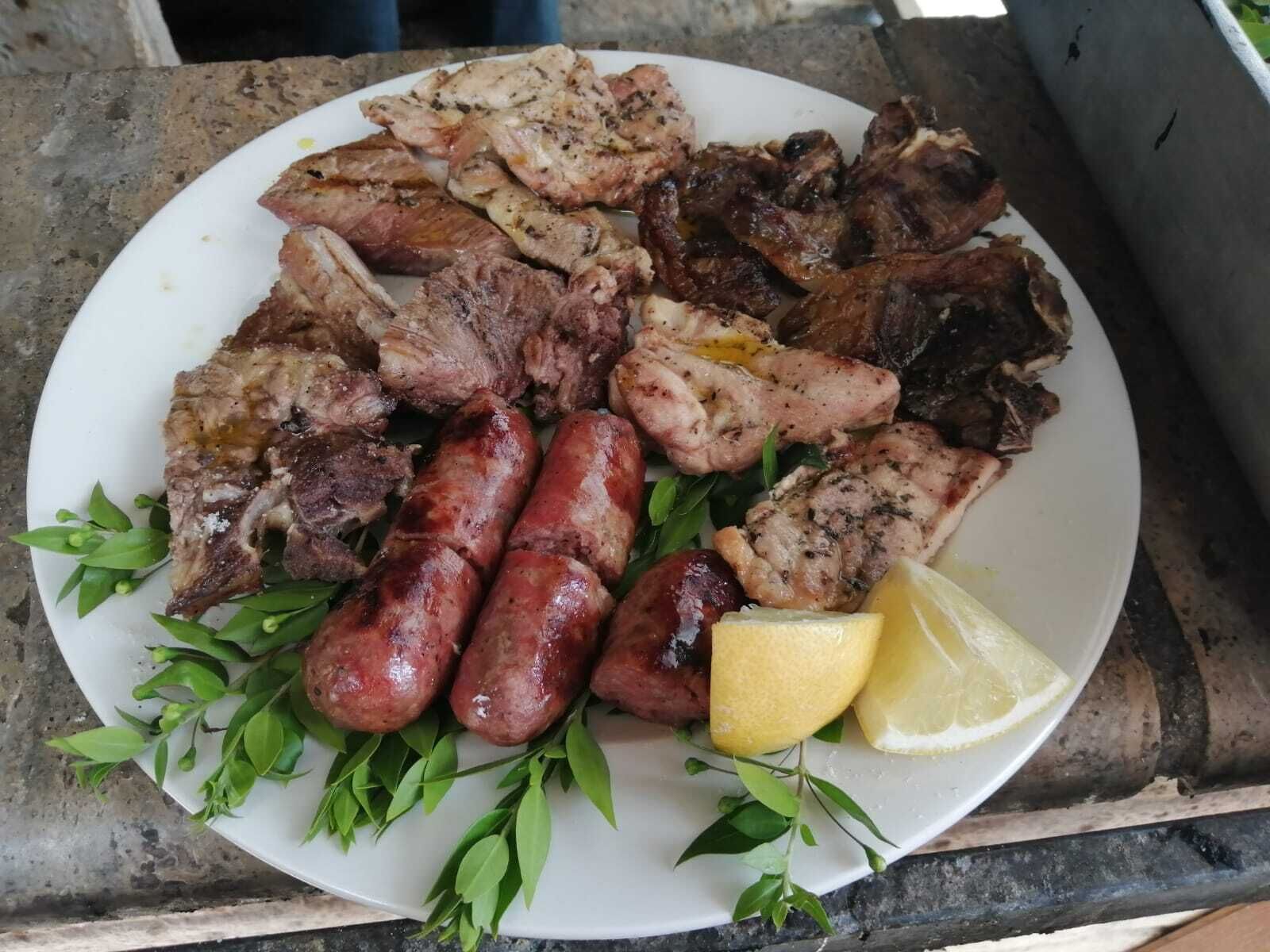 Un plat de carns i salsitxes a la planxa, decorat amb fulles verdes i rodanxes de llimona.