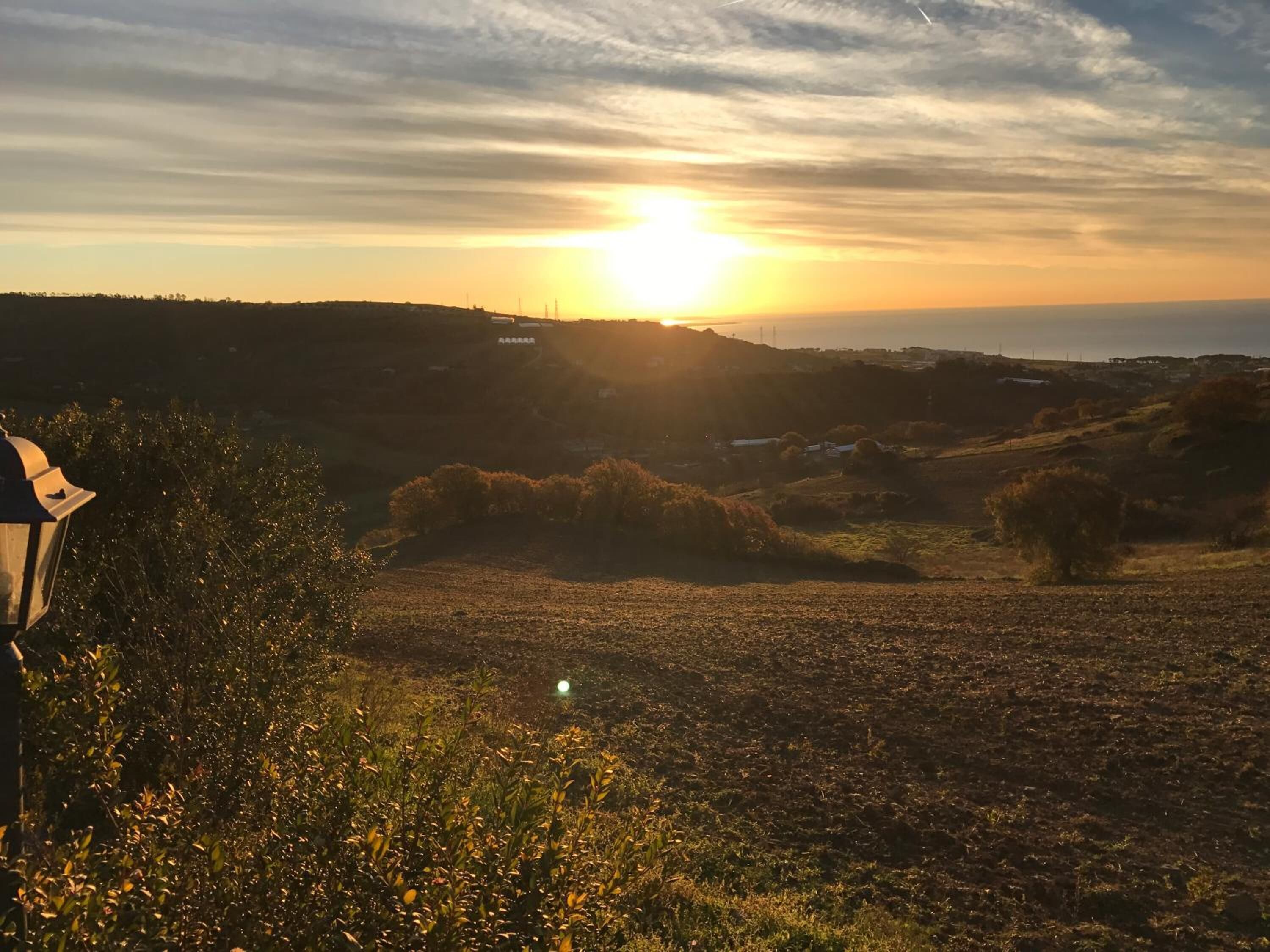 Tramonto su un paesaggio collinare, con un lampione in primo piano.