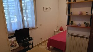 A bedroom with a bed, a desk with a laptop, a radiator, and a shelf with decorative items. - I Cardinali (Santa Marinella)