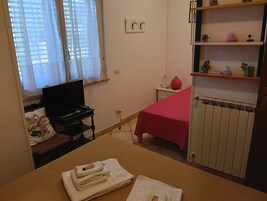 Una camera da letto con un letto, una scrivania con un portatile, un termosifone e una mensola con oggetti decorativi.