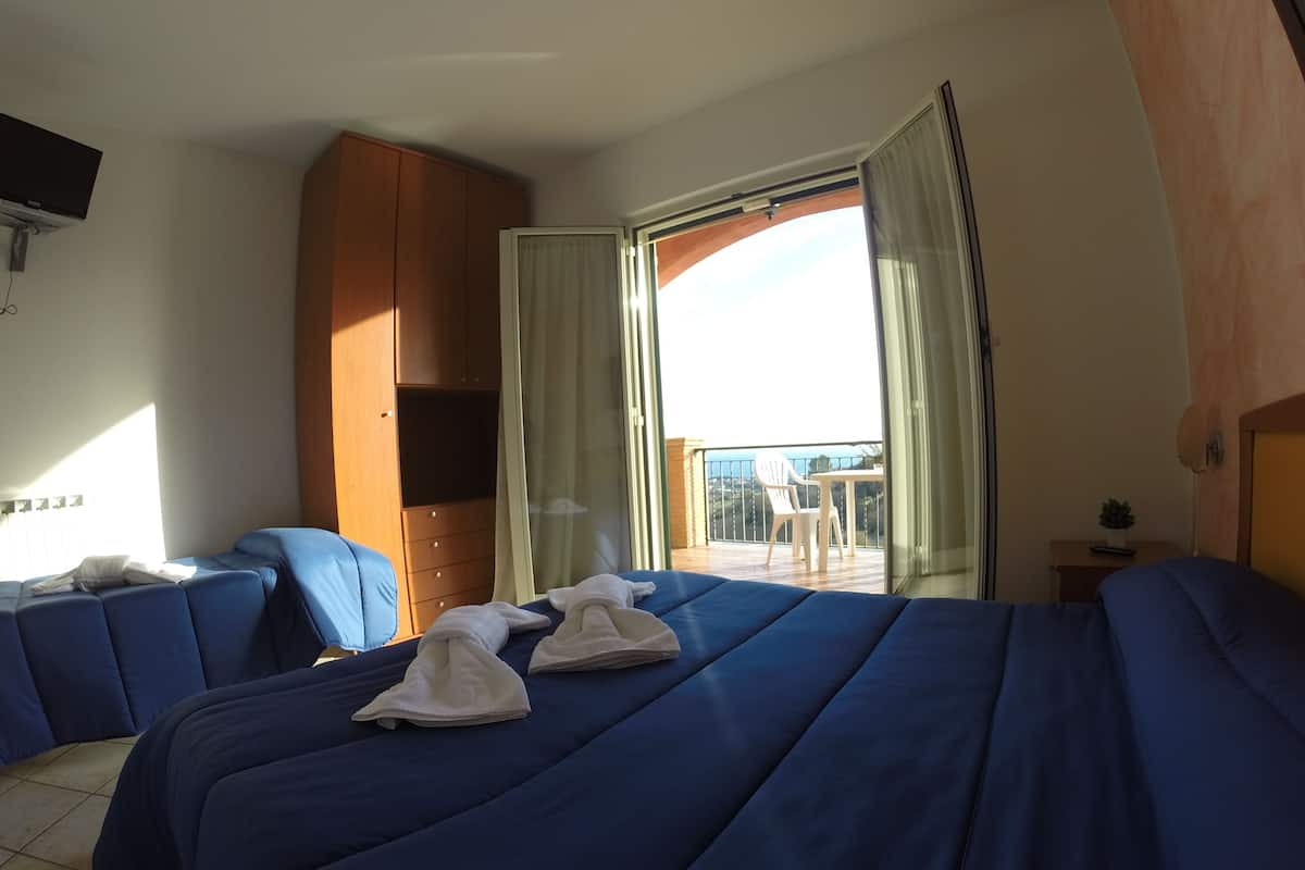 Ein Hotelzimmer mit zwei Betten, einem Holzschrank, einem Balkon mit Tisch und Stühlen sowie einem an der Wand befestigten Fernseher.