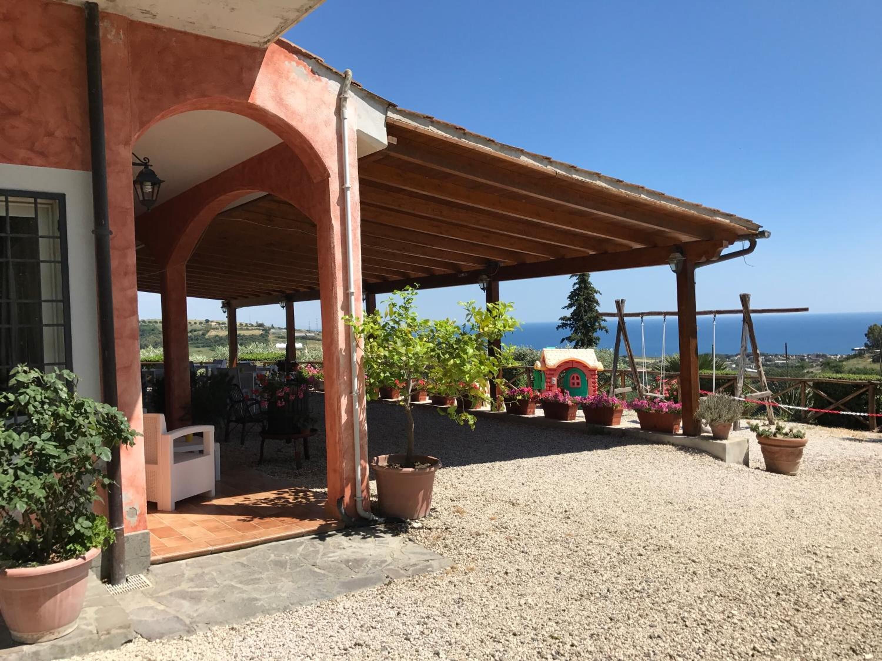 Un espace extérieur aménagé en terrasse, avec une pergola, des plantes en pot et une vue sur la mer.