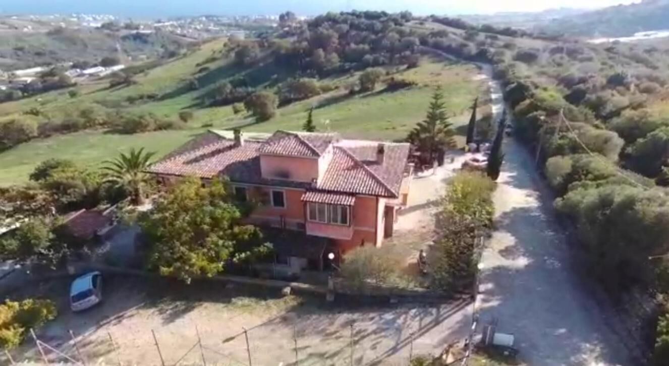 A house with a red roof, surrounded by greenery and a river.