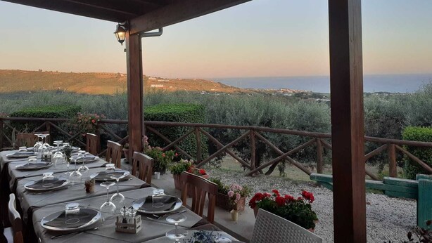 An outdoor dining area with tables set for a meal, overlooking a scenic landscape with hills and a view of the sea. - I Cardinali (Santa Marinella)