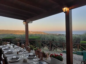 An outdoor dining area with tables set for a meal, overlooking a scenic landscape with hills and a view of the sea. - I Cardinali (Santa Marinella)