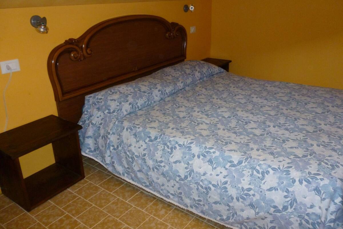A bedroom with a wooden headboard, a floral bedspread, and a nightstand on one side.