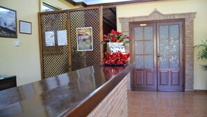 A reception area with a wooden reception desk, a bulletin board with notices, a door with glass panels, and a potted plant. - La Encina Centenaria (Monachil)