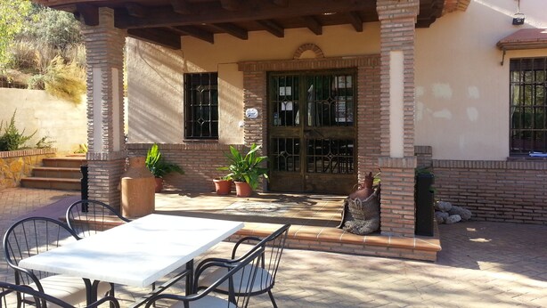 A patio area with a table and chairs, a covered seating area, and a building with a tiled roof and brick walls. - La Encina Centenaria (Monachil)