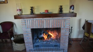 A brick fireplace with a wooden mantel, a cat bed, and decorative items. - La Encina Centenaria (Monachil)