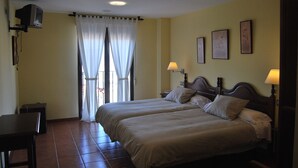 A bedroom with two beds, a TV mounted on the wall, and a small table. - La Encina Centenaria (Monachil)