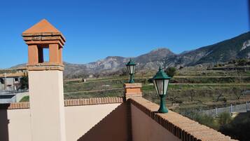 Una terraza con vistas a montañas, un muro de ladrillo y dos farolas verdes.