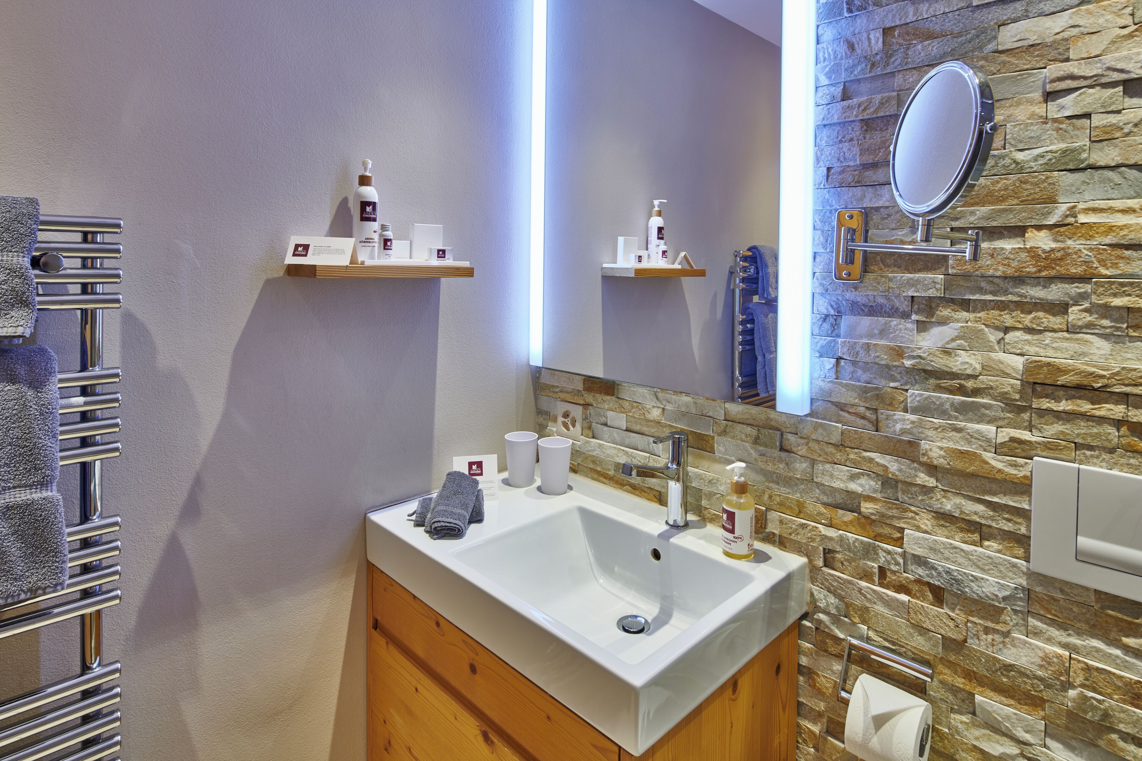 A bathroom with a white sink, a mirror, a towel rack, and a stone wall.
