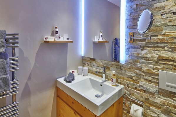 A bathroom with a white sink, a mirror, a towel rack, and a stone wall.
