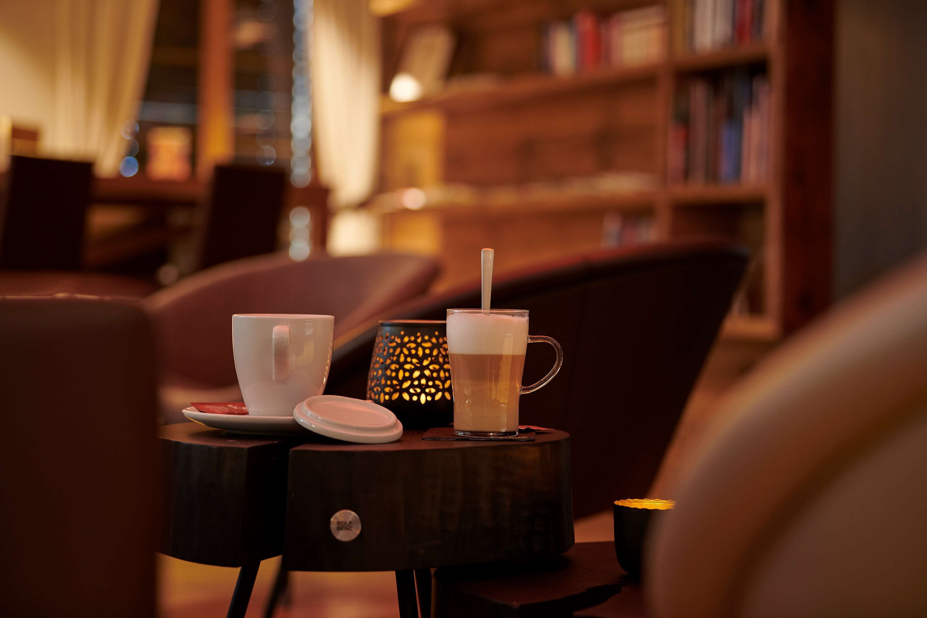 A cozy seating area with a table holding a cup and a mug, a small lamp, and a book on a side table.