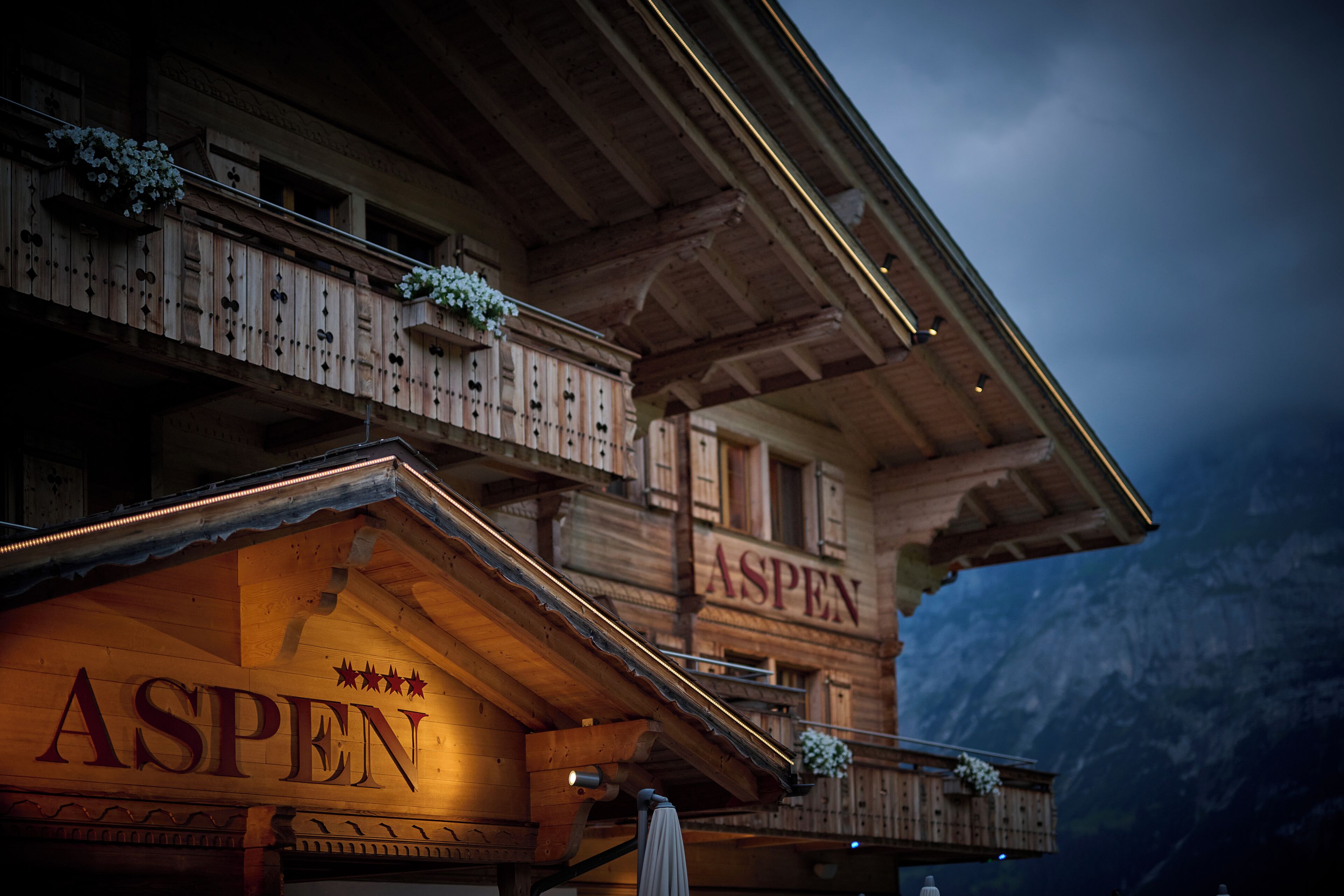 Un edificio de madera con balcones, un letrero que dice 'ASPEN' y un paisaje montañoso de fondo.