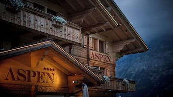 Un edificio de madera con balcones, un letrero que dice 'ASPEN' y un paisaje montañoso de fondo.