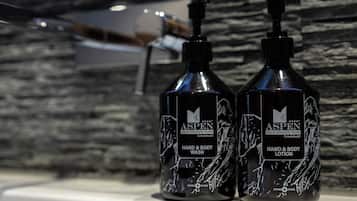 Two bottles of Aspen hand and body wash on a white surface with a stone wall background.