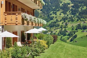 A hotel with a balcony, outdoor seating, and a view of a green valley.