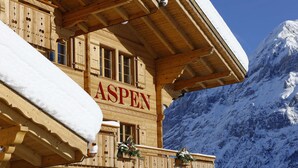 A wooden building with the name "ASPEN" on the facade, featuring a balcony with railings and windows.