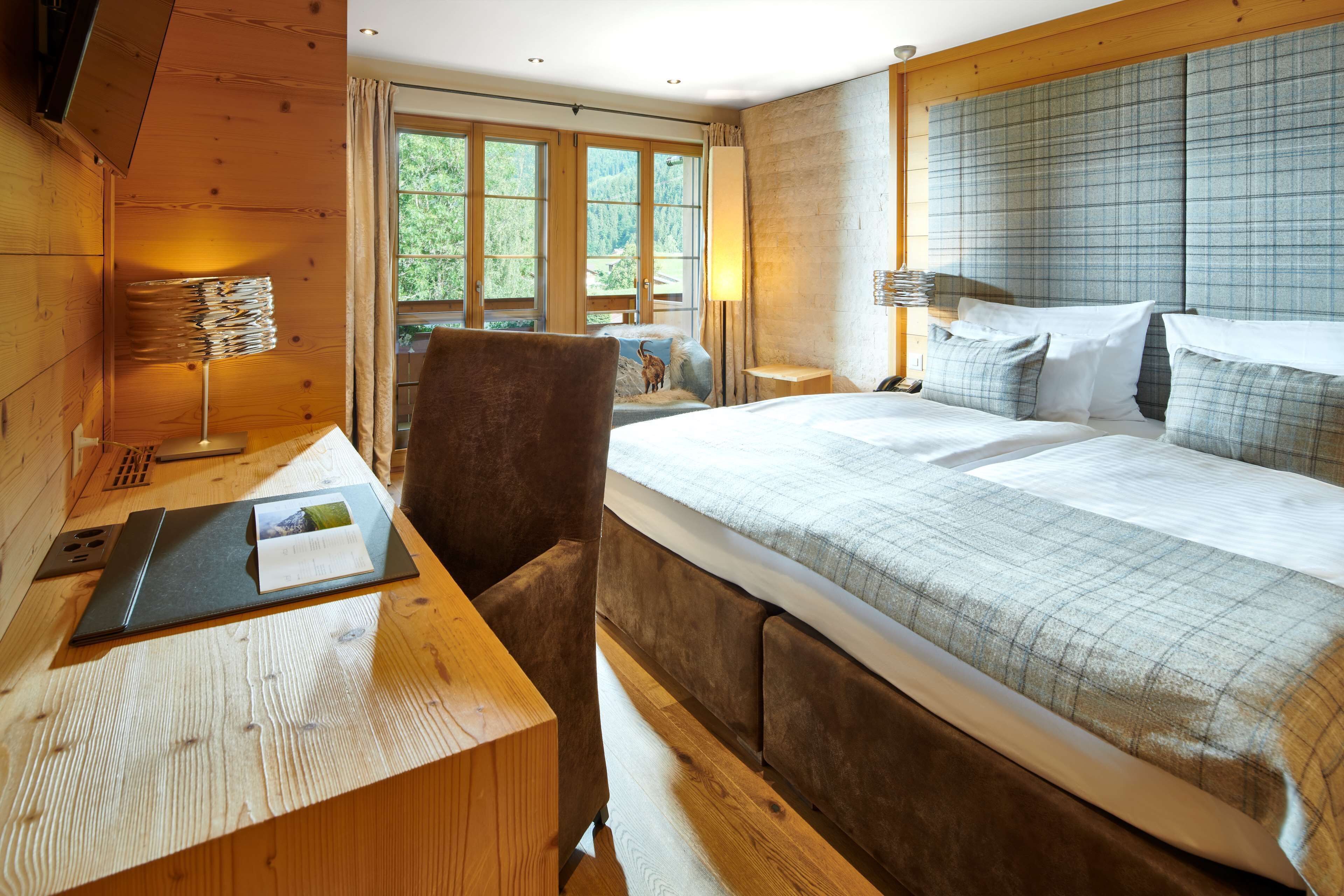 A bedroom with a large bed, wooden walls, and a desk with a lamp.