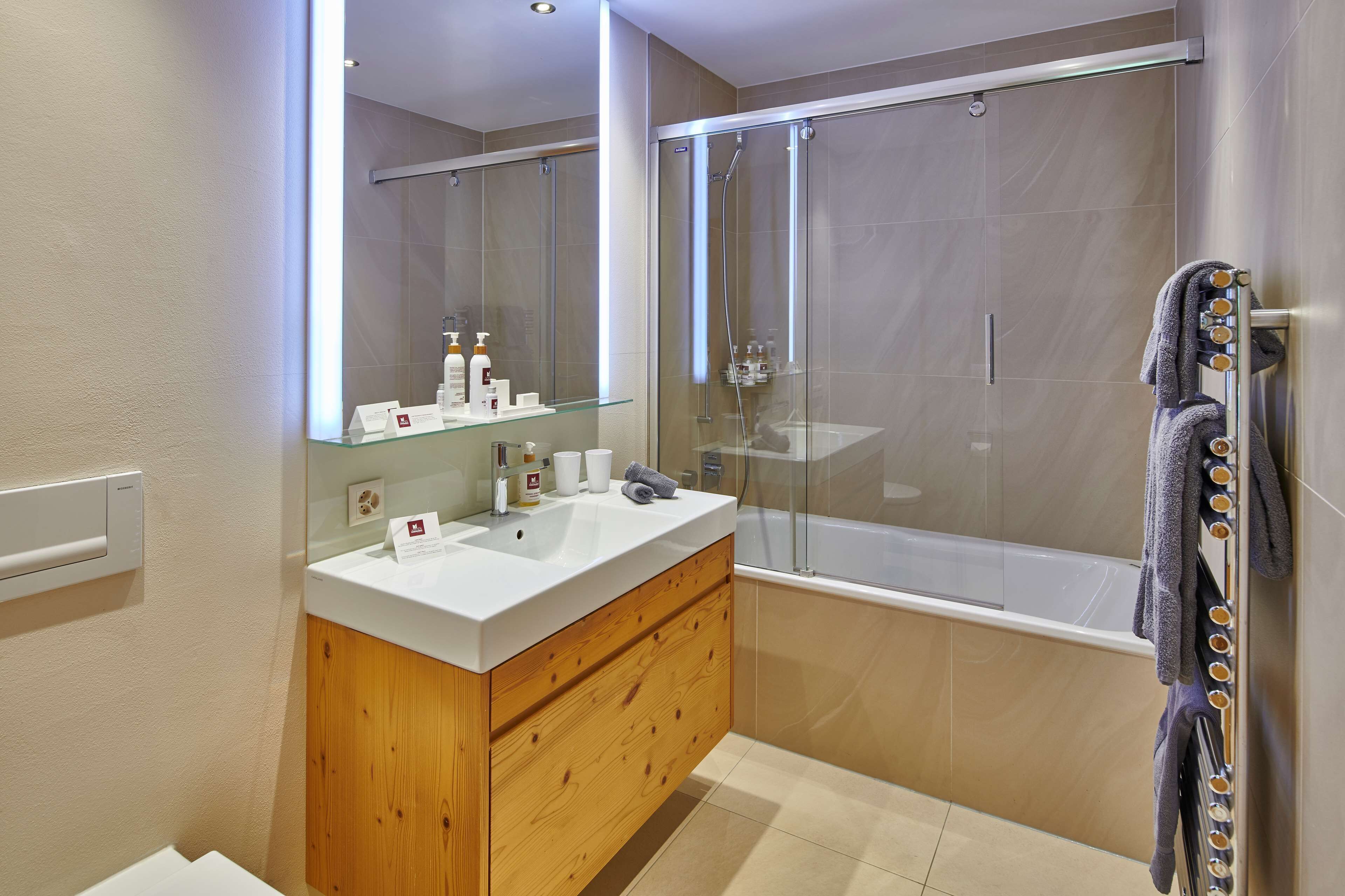 Un baño moderno con ducha envuelta en vidrio, tocador de madera con lavamanos blanco y un espejo grande.