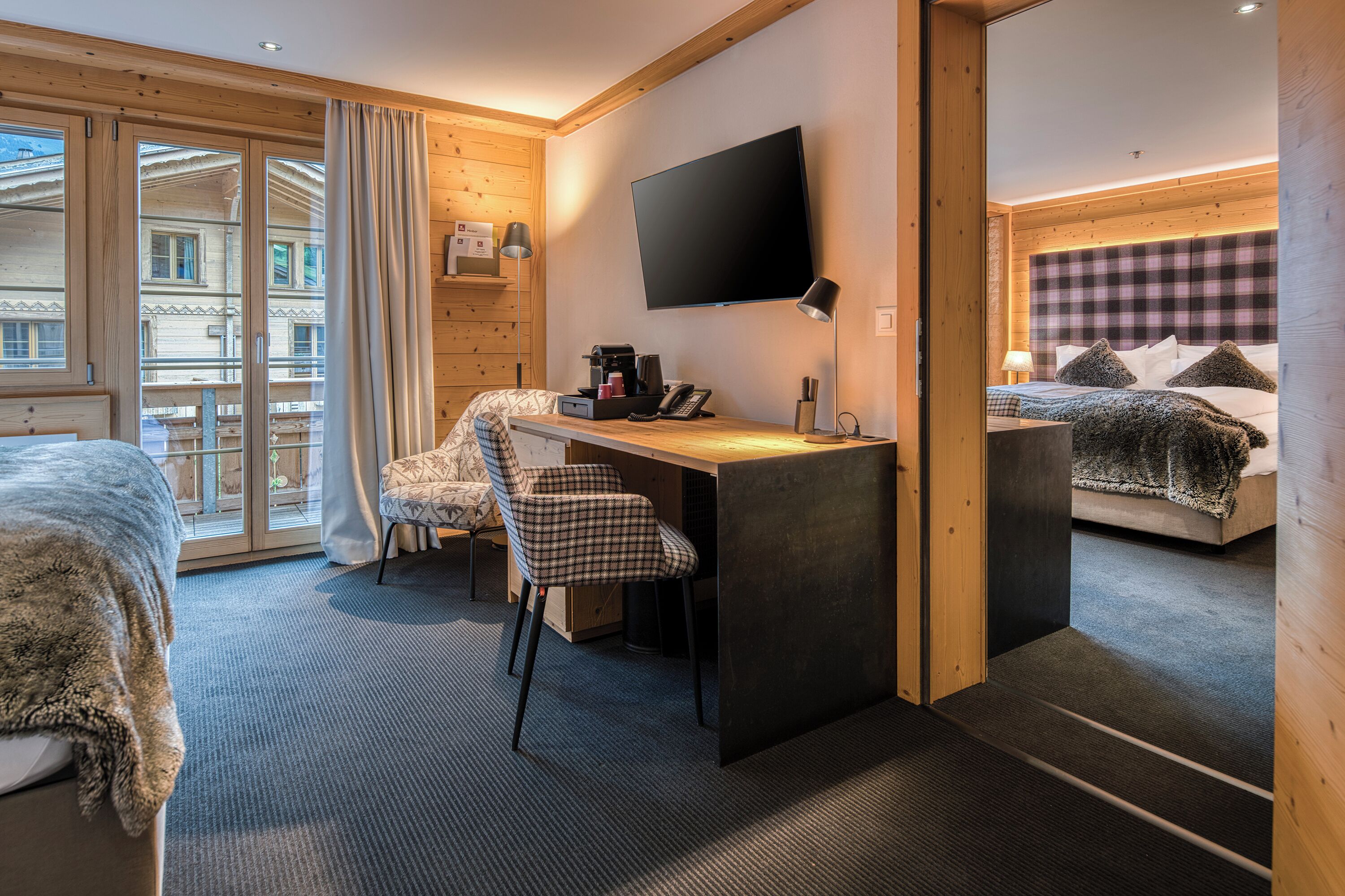 Habitación de hotel con cama, escritorio, silla, televisión y vistas al exterior.