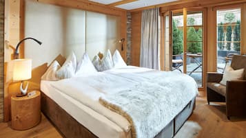 Una cama grande con una manta blanca esponjosa, una mesita de noche de madera con una lámpara y vistas a un balcón con mobiliario exterior.