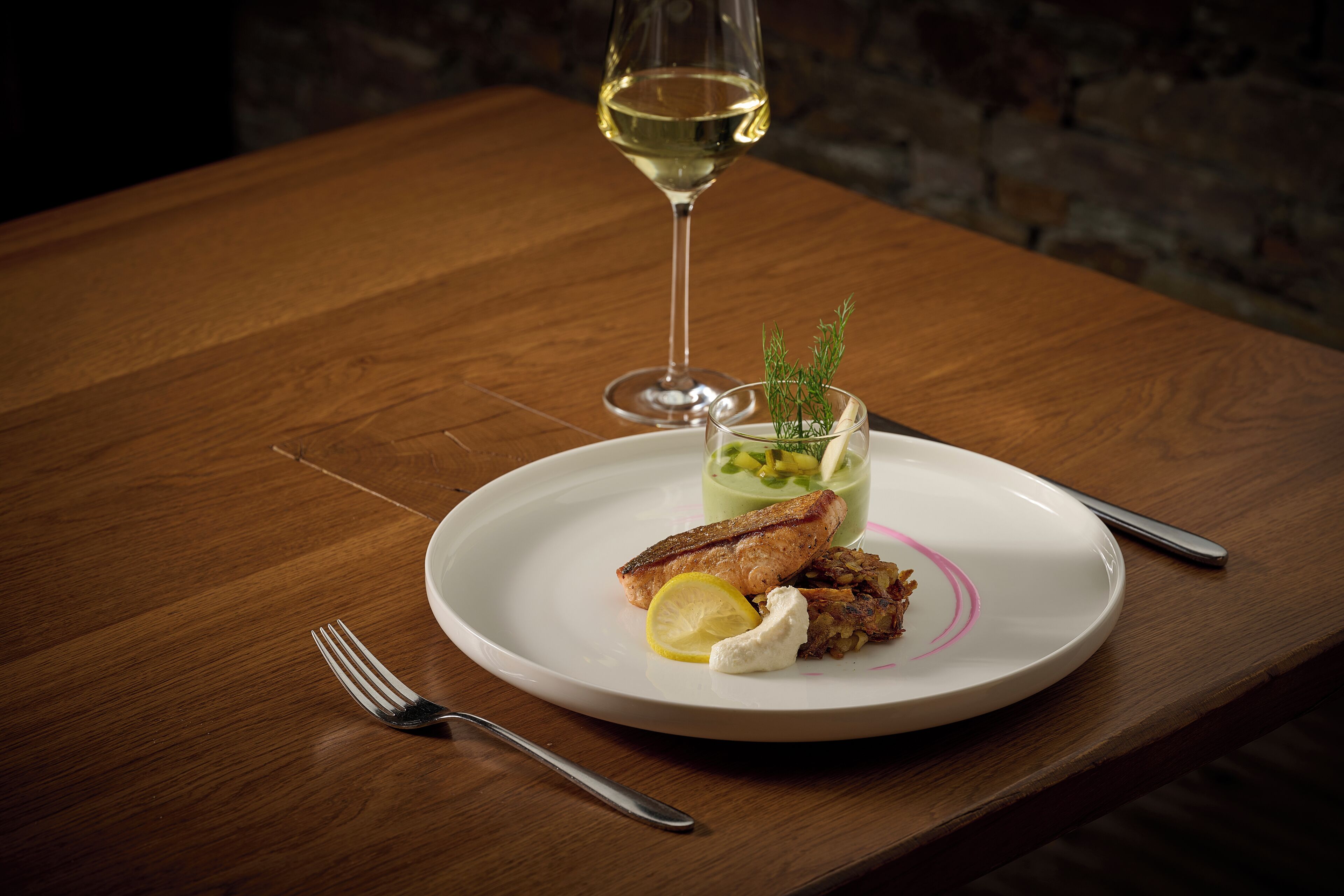 Een bord eten met een glas witte wijn op een houten tafel.