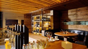 A bar area with a wooden ceiling, shelves with bottles, a bar counter, and a round table with a candle.