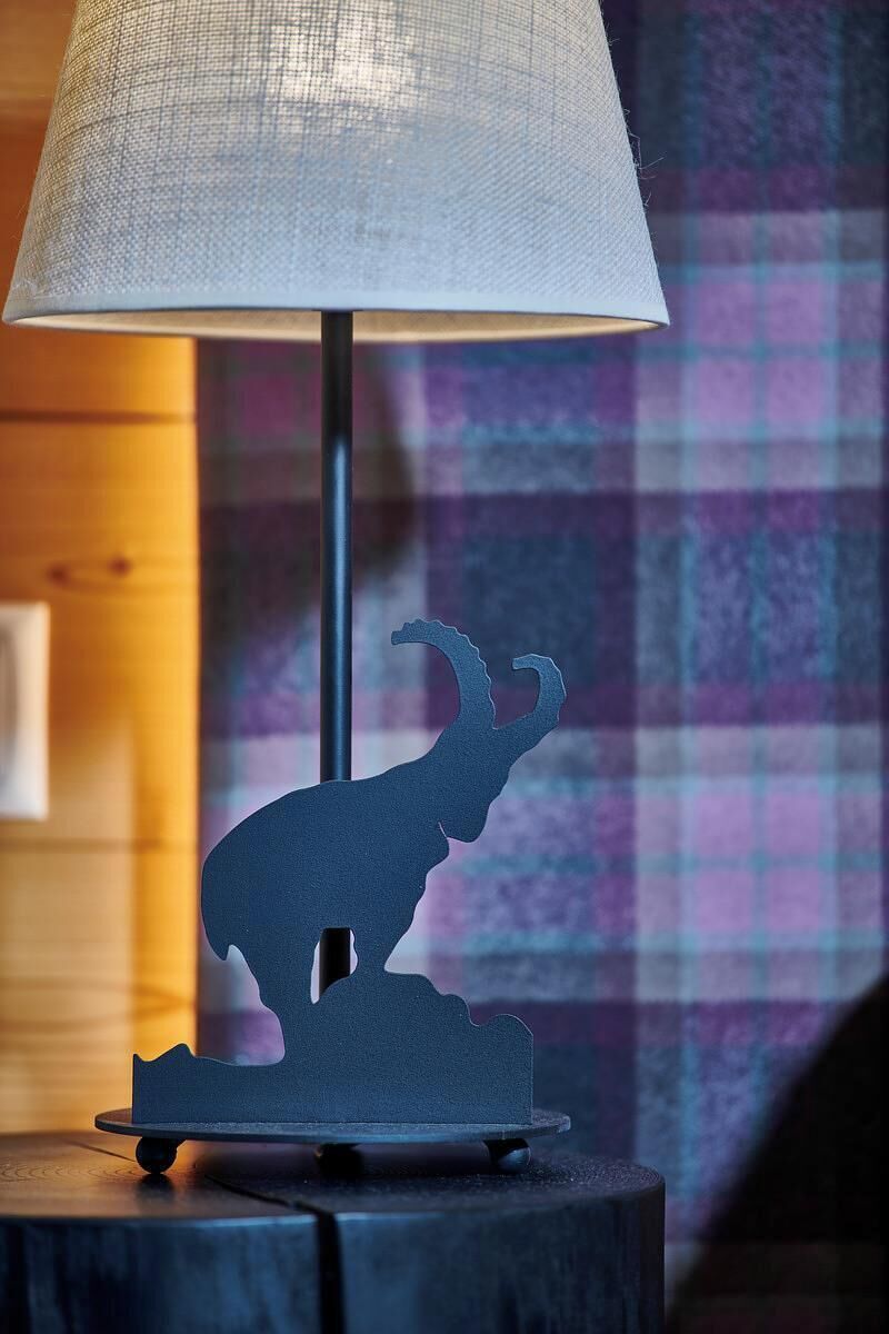 Een lamp met een silhouet van een lama op een houten voet, geplaatst op een tafel met een geruit motief.