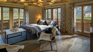 A spacious bedroom with a large bed, a sitting area with a chair, and a view of the mountains through large windows.