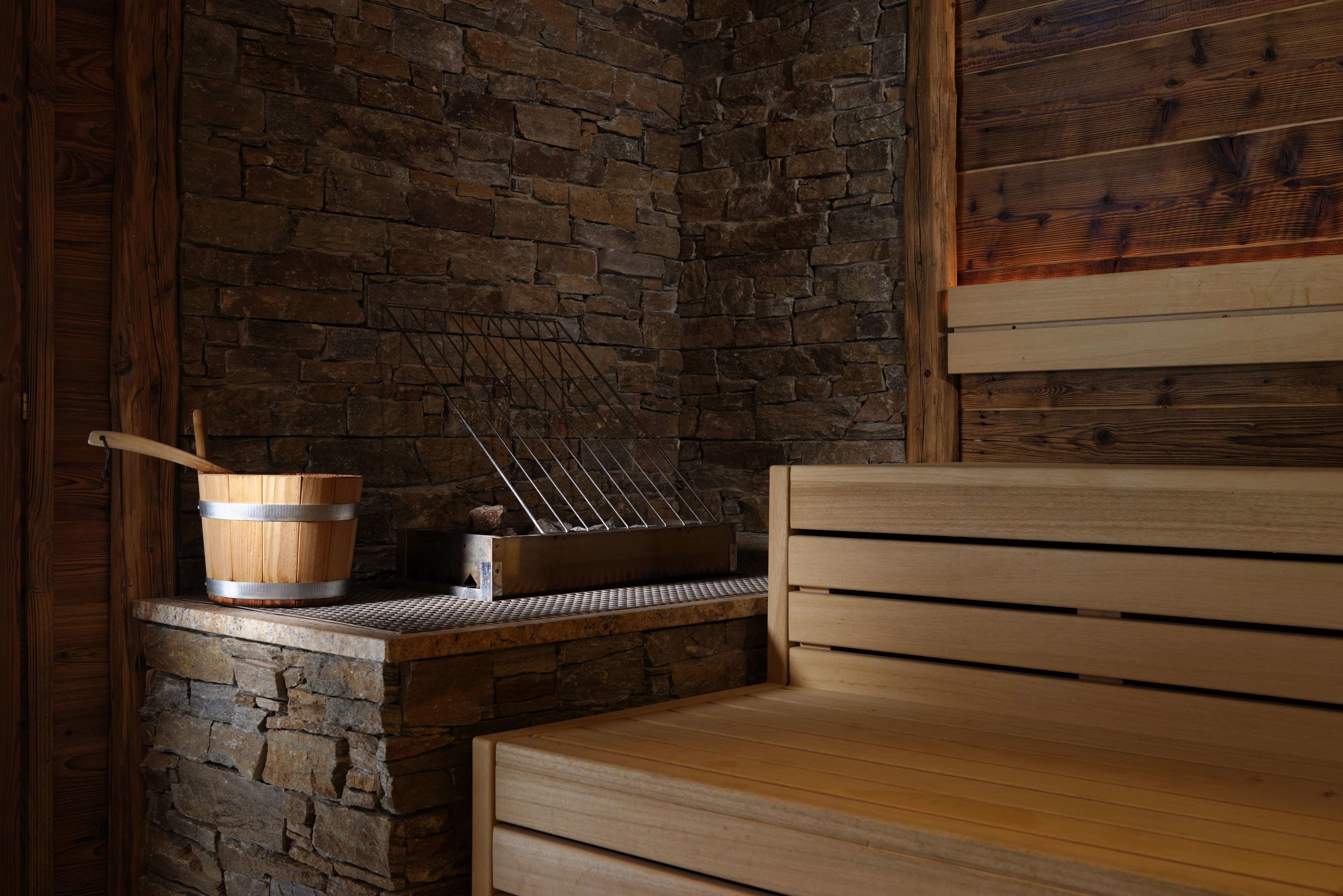 Sauna, jossa on puinen penkki, kiviseinä ja metallinen teline pyyhkeille.