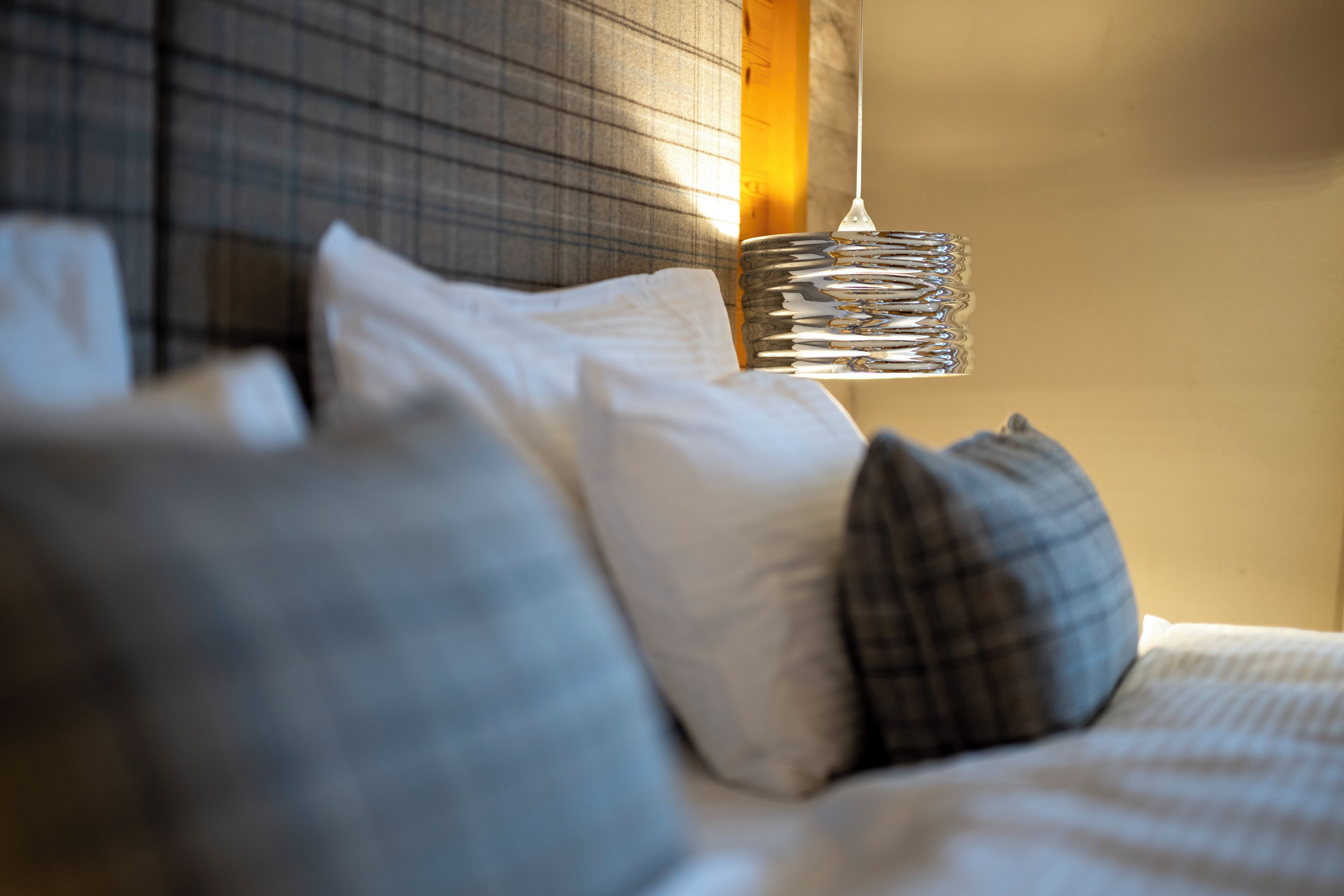 A bed with white and grey pillows, a hanging light fixture, and a textured wall.