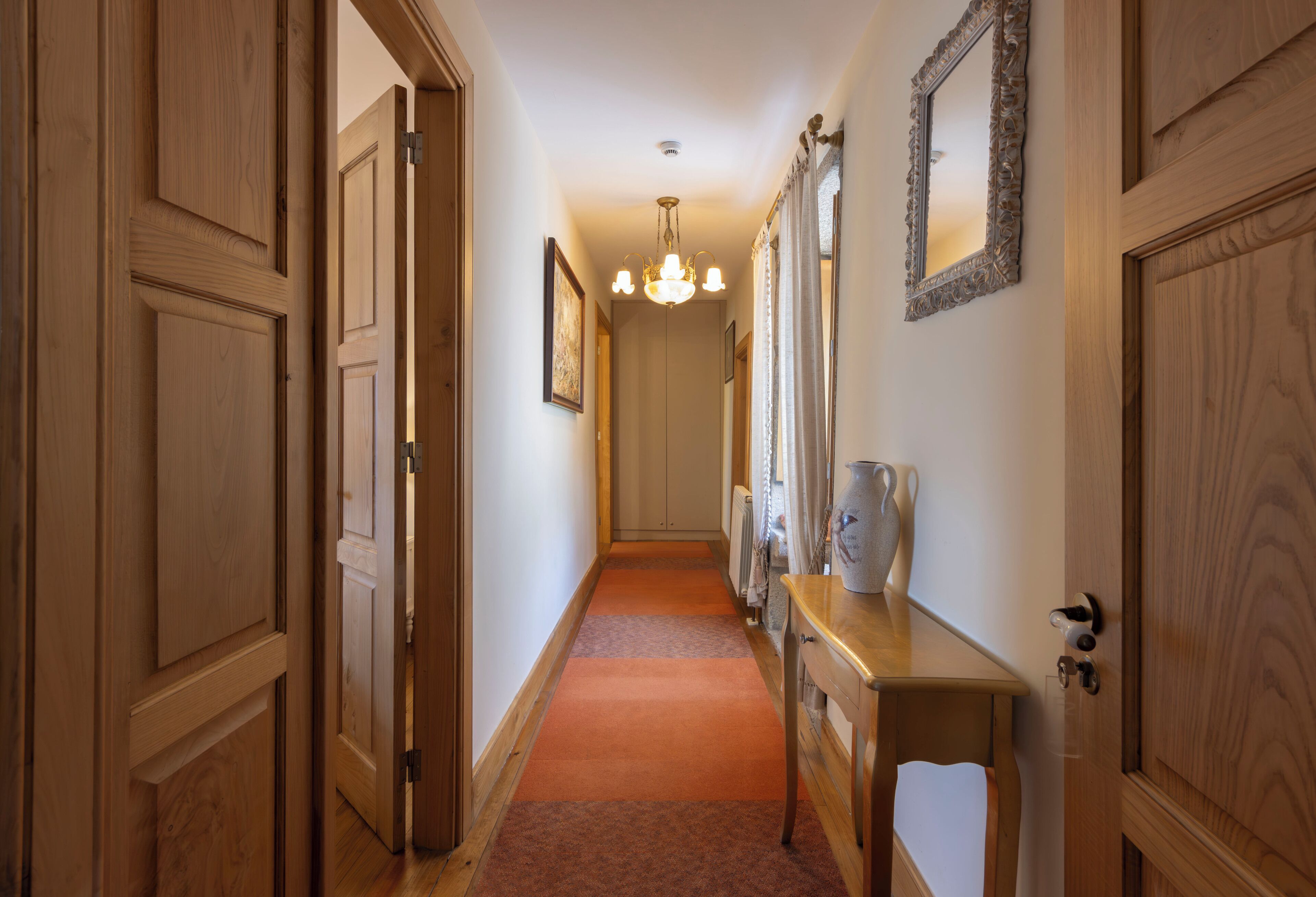 Un couloir avec des portes en bois, une commode en bois et un lustre.