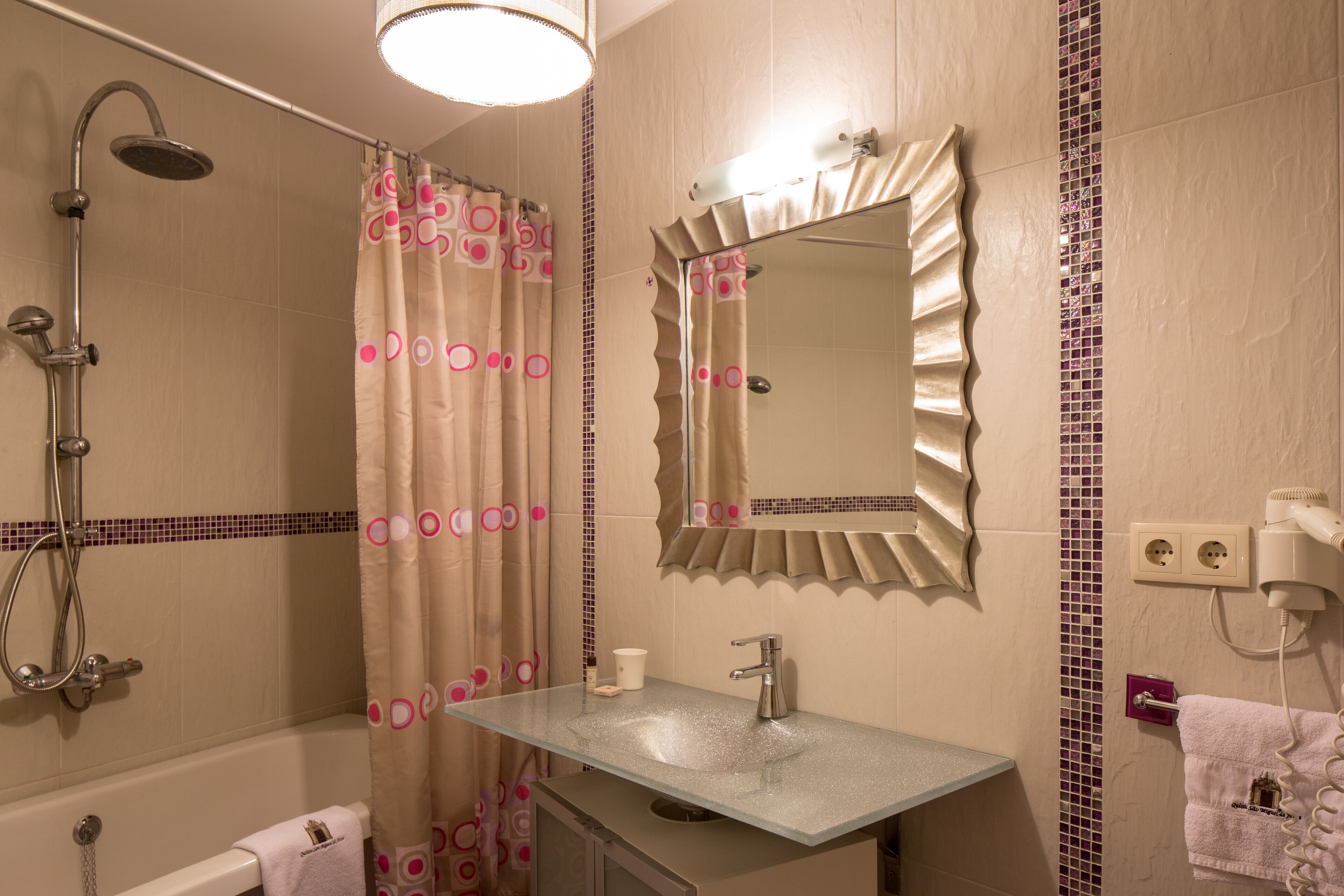A bathroom with a shower, a sink, a mirror, and a towel rack.