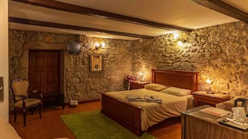 A bedroom with a stone wall, wooden bed, bedside tables, a chair, and a green rug.