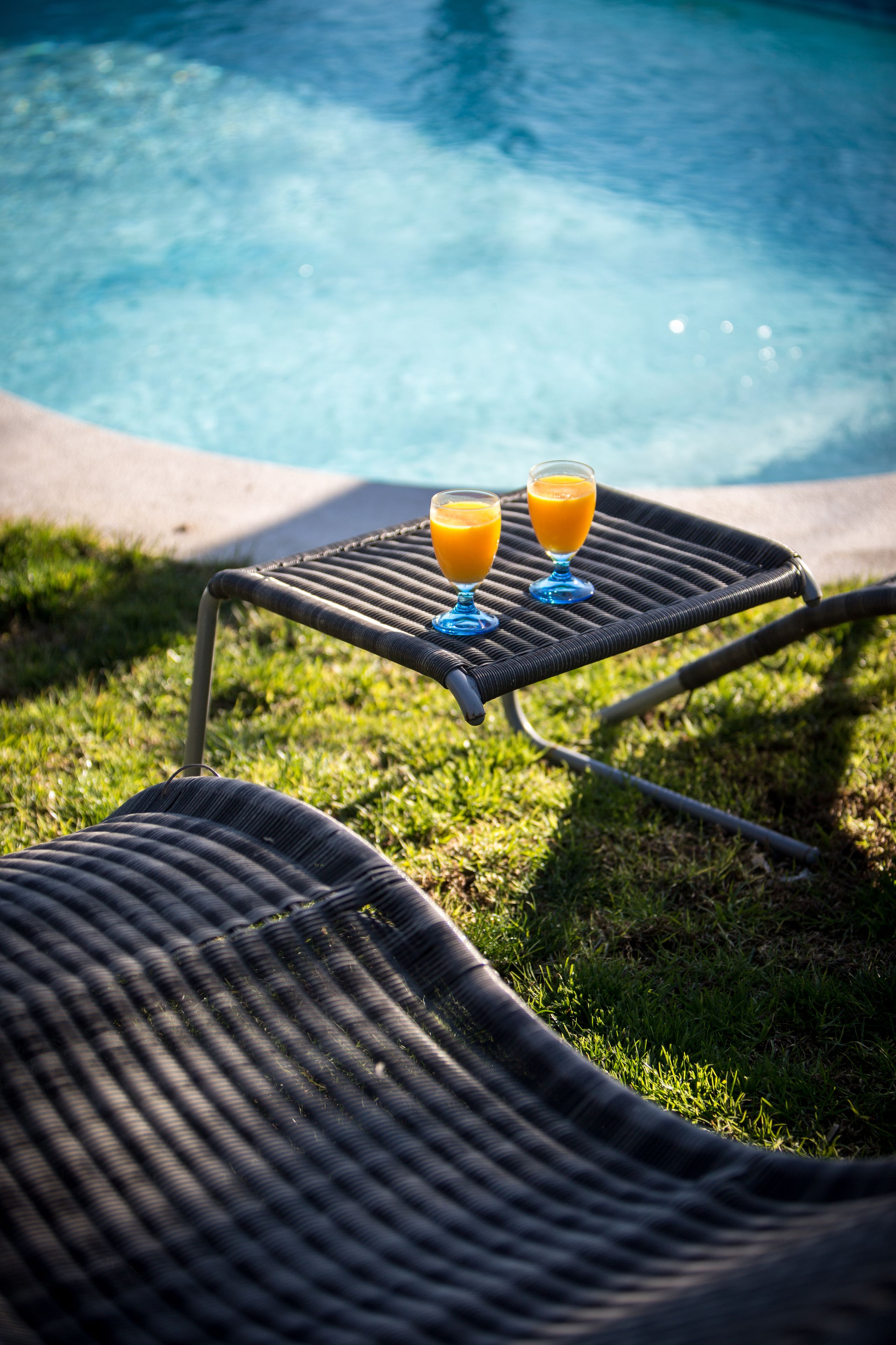 A poolside area with two lounge chairs and two glasses of orange juice on a table.